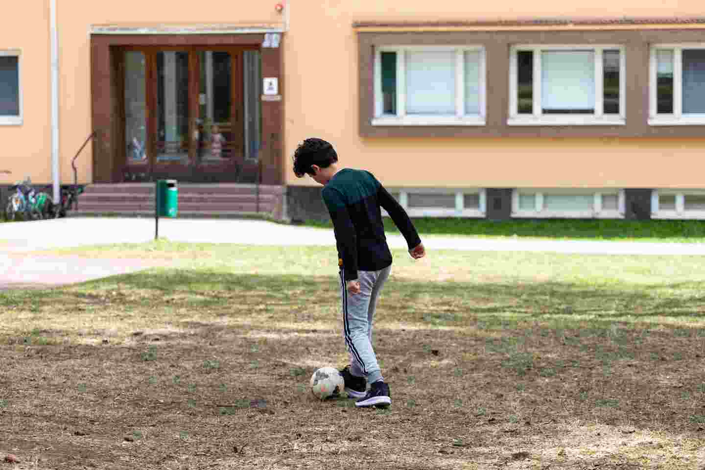 Nuori henkilö potkaisemassa jalkapalloa vastaanottokeskuksen pihalla.